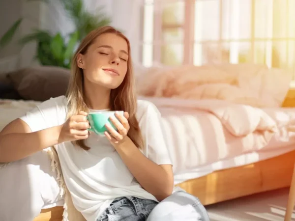 A woman sitting on the floor, drinking coffee.