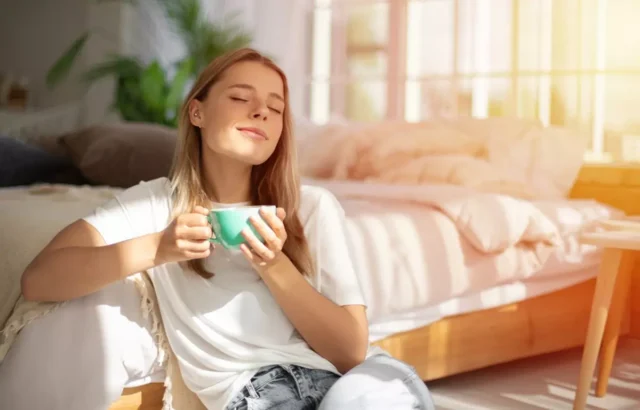 A woman sitting on the floor, drinking coffee.